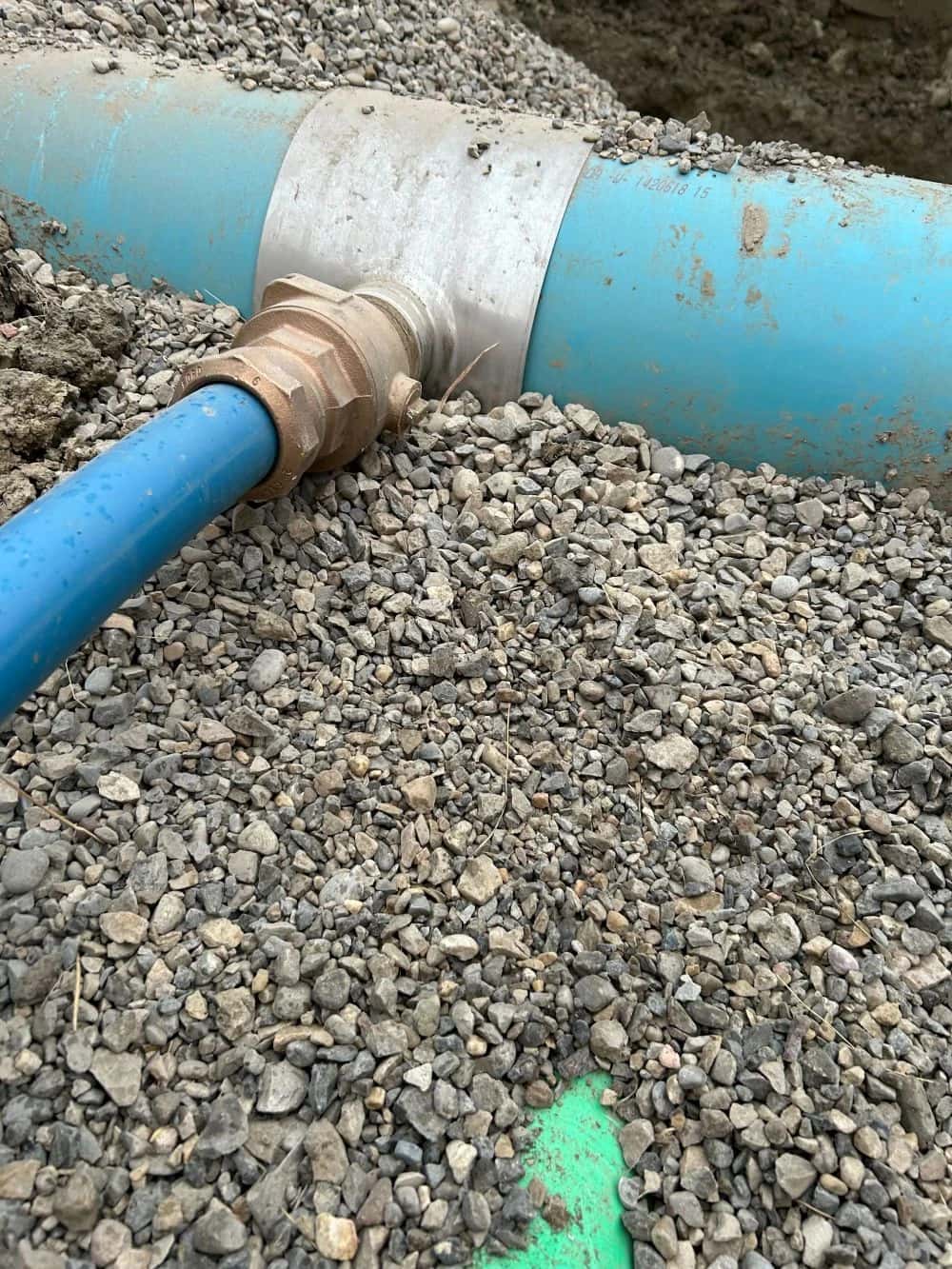 Brass saddle tap and service line on a blue PVC watermain in gravel bedding