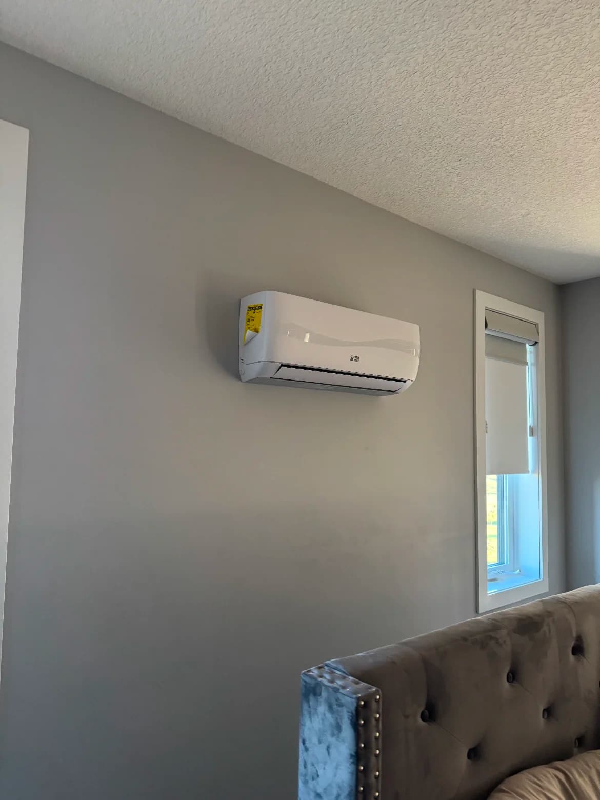 Ductless mini-split head mounted on a grey bedroom wall beside a window