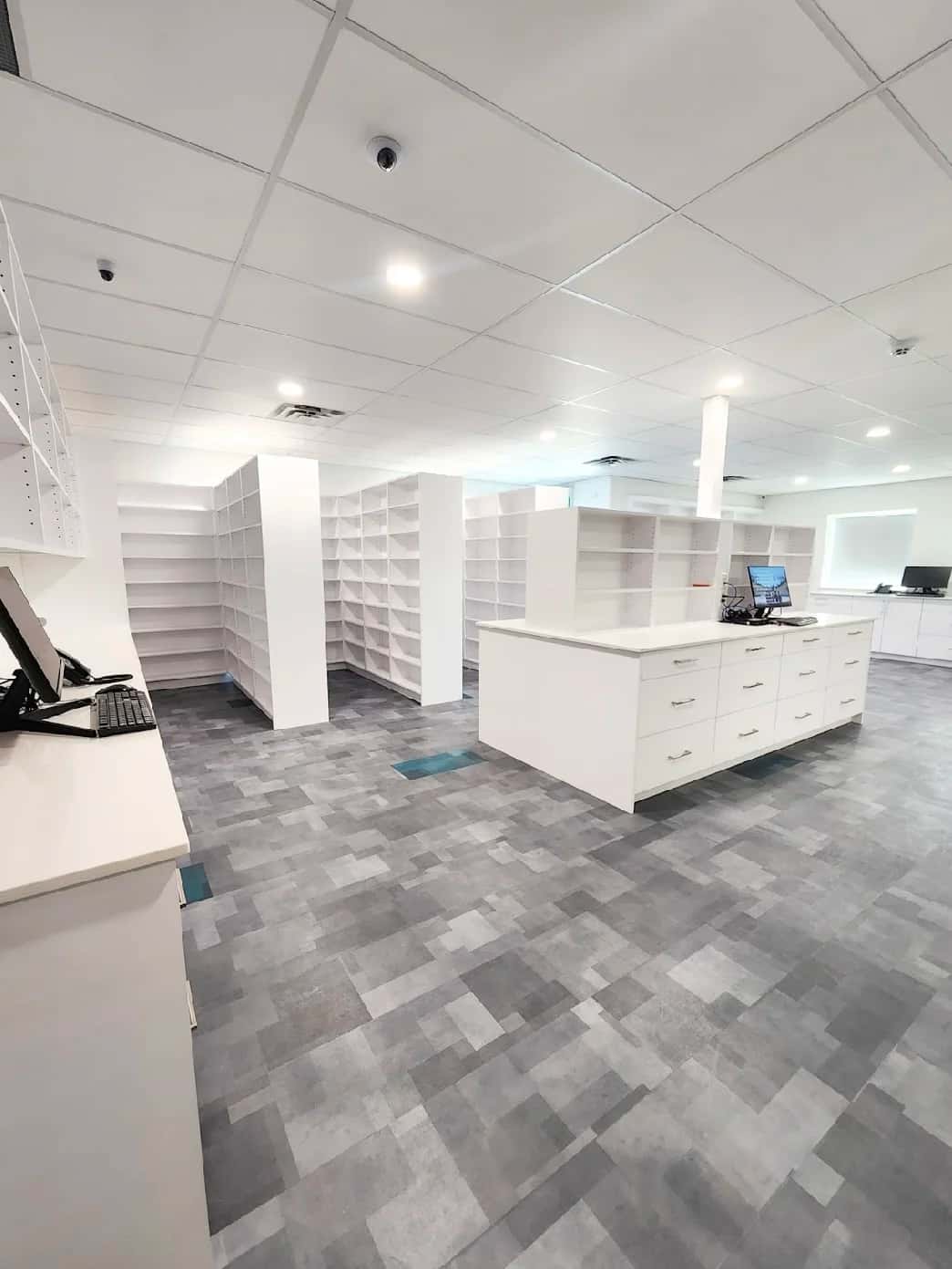 White pharmacy dispensary millwork and open shelving over checkered vinyl plank flooring