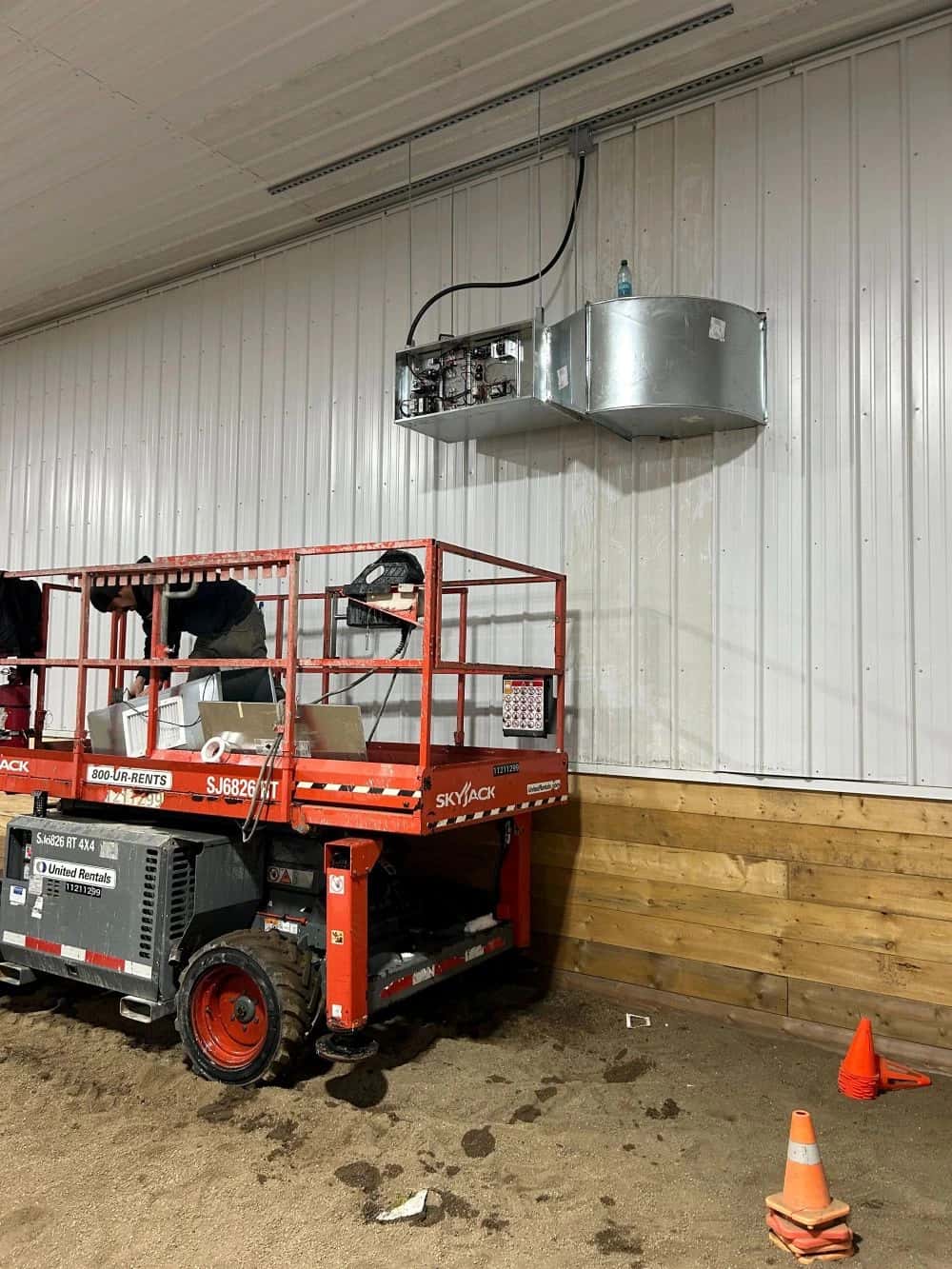 Crew on a scissor lift installing a wall-mounted sheet-metal air unit in a metal building