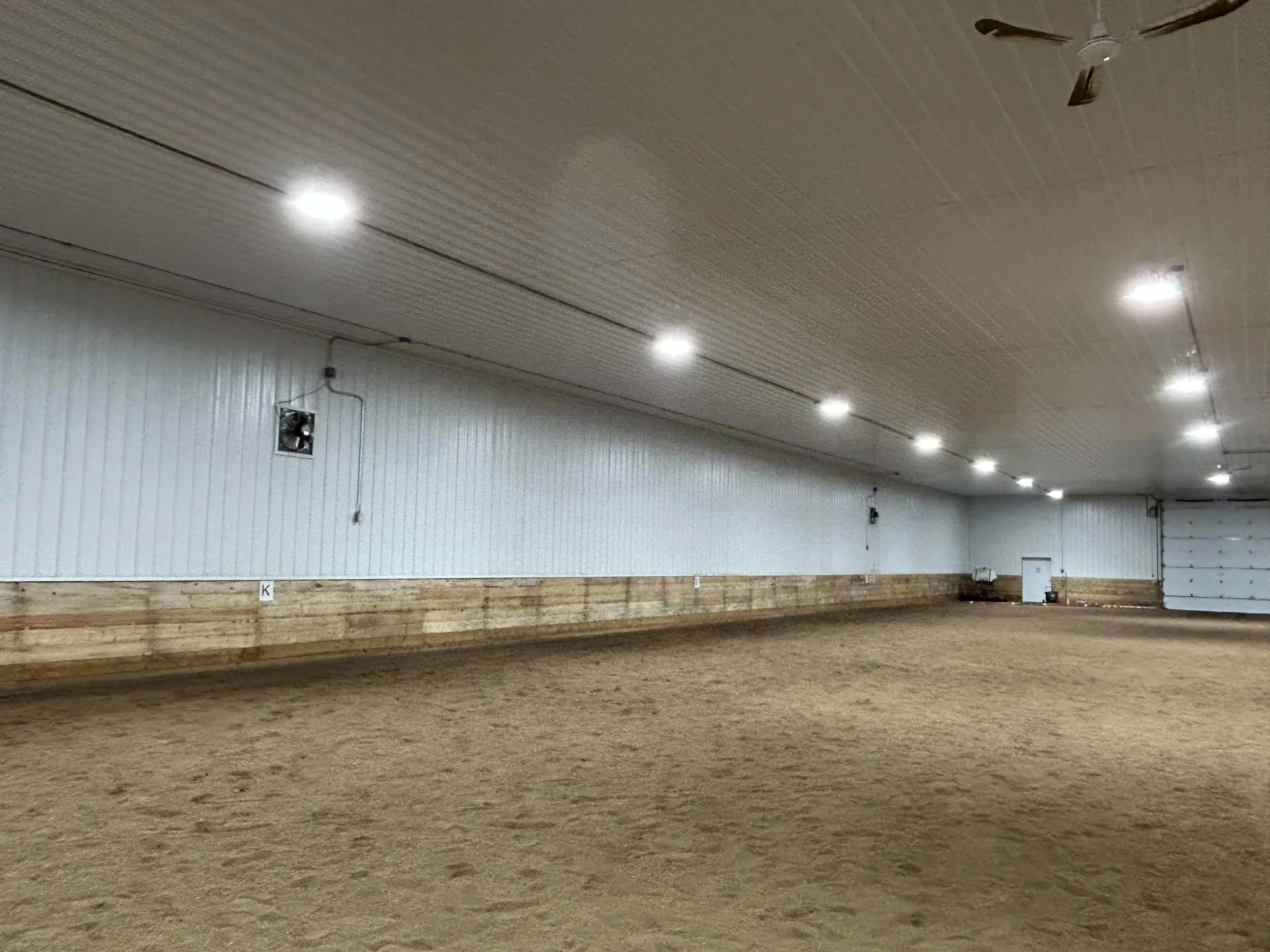 Finished indoor riding arena with white liner panels, wood kickboards and rows of LED lights