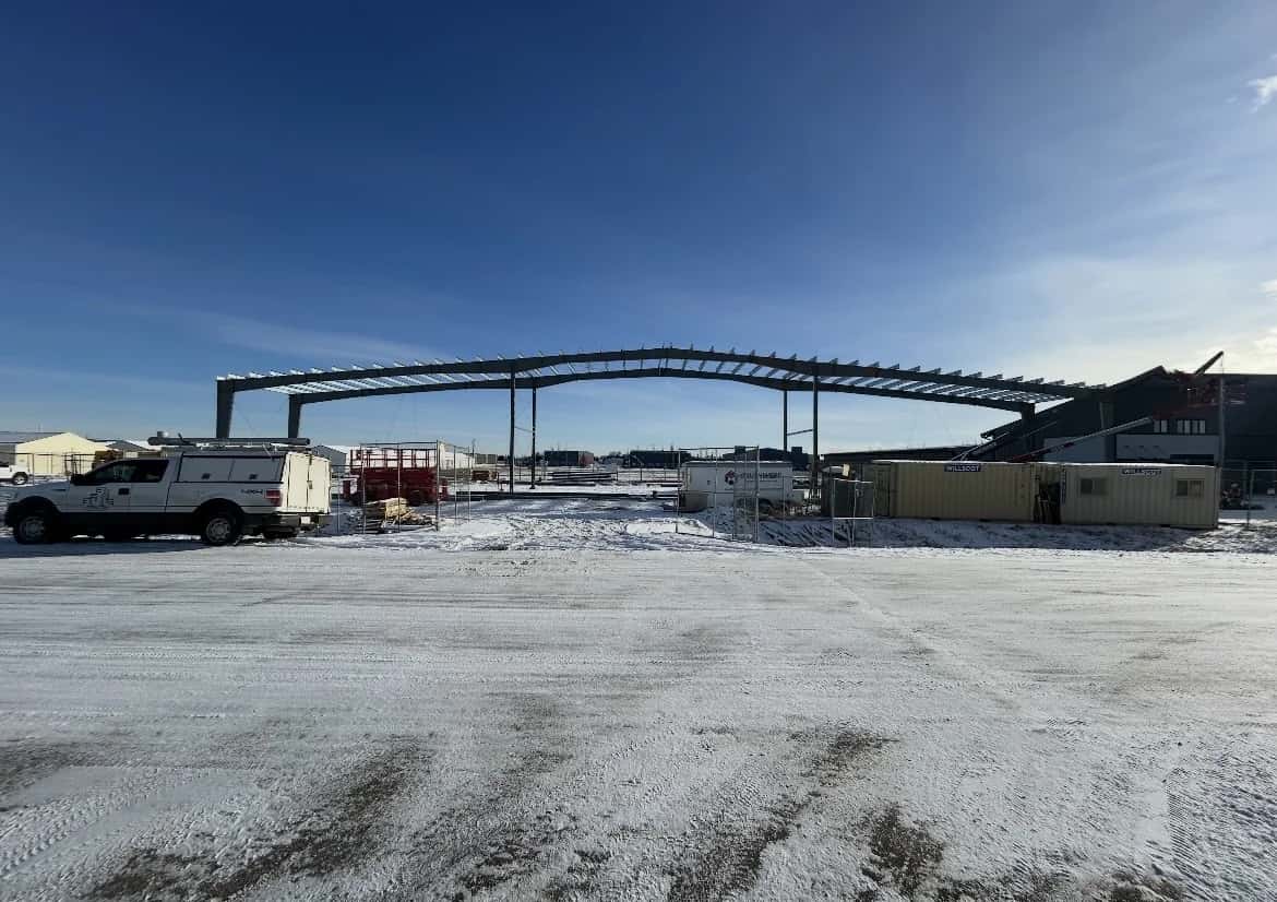 Clear-span steel building skeleton rising over a snowy industrial site