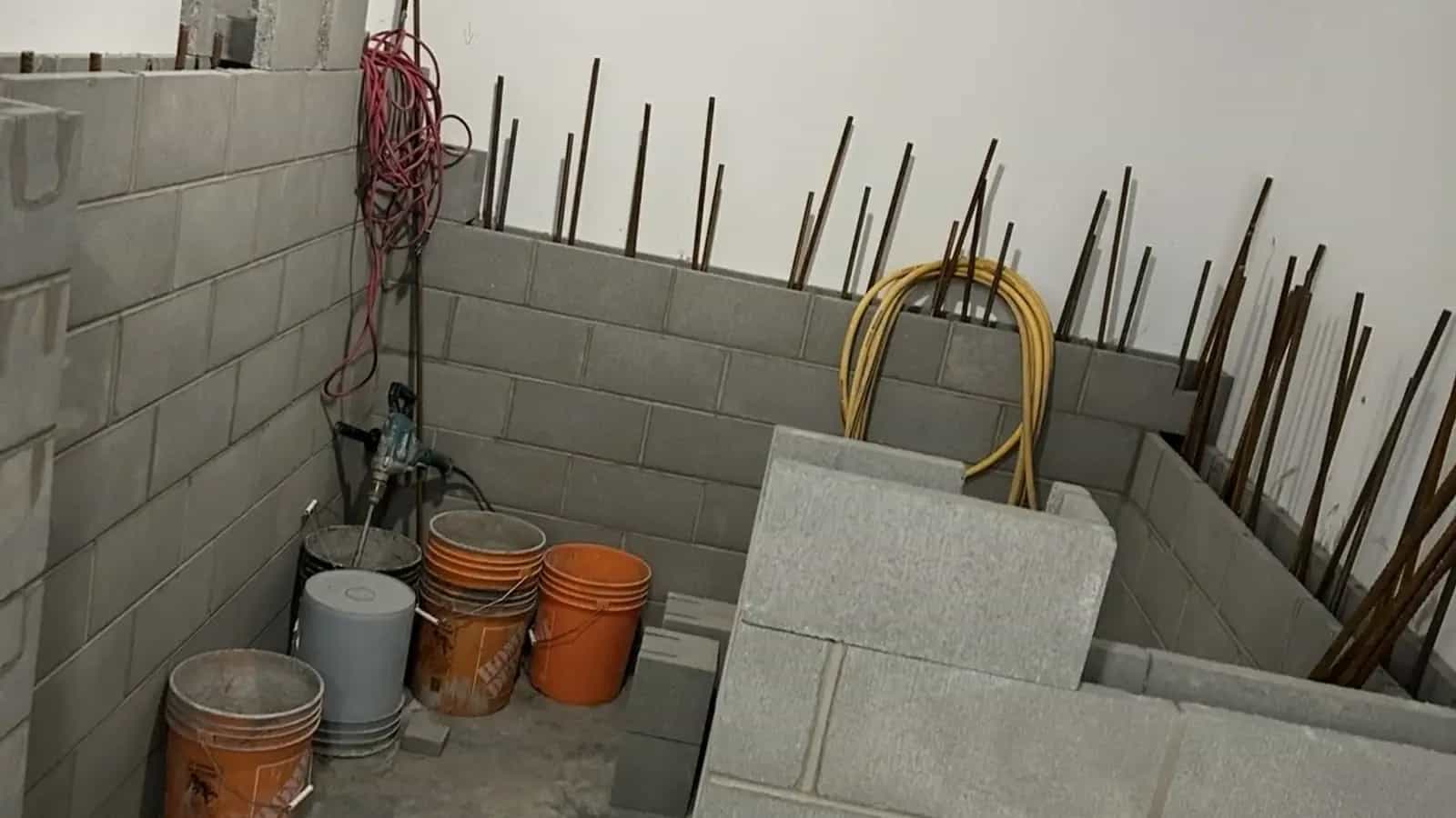 Concrete-block core walls mid-build with rebar dowels, grout buckets and a mixing drill