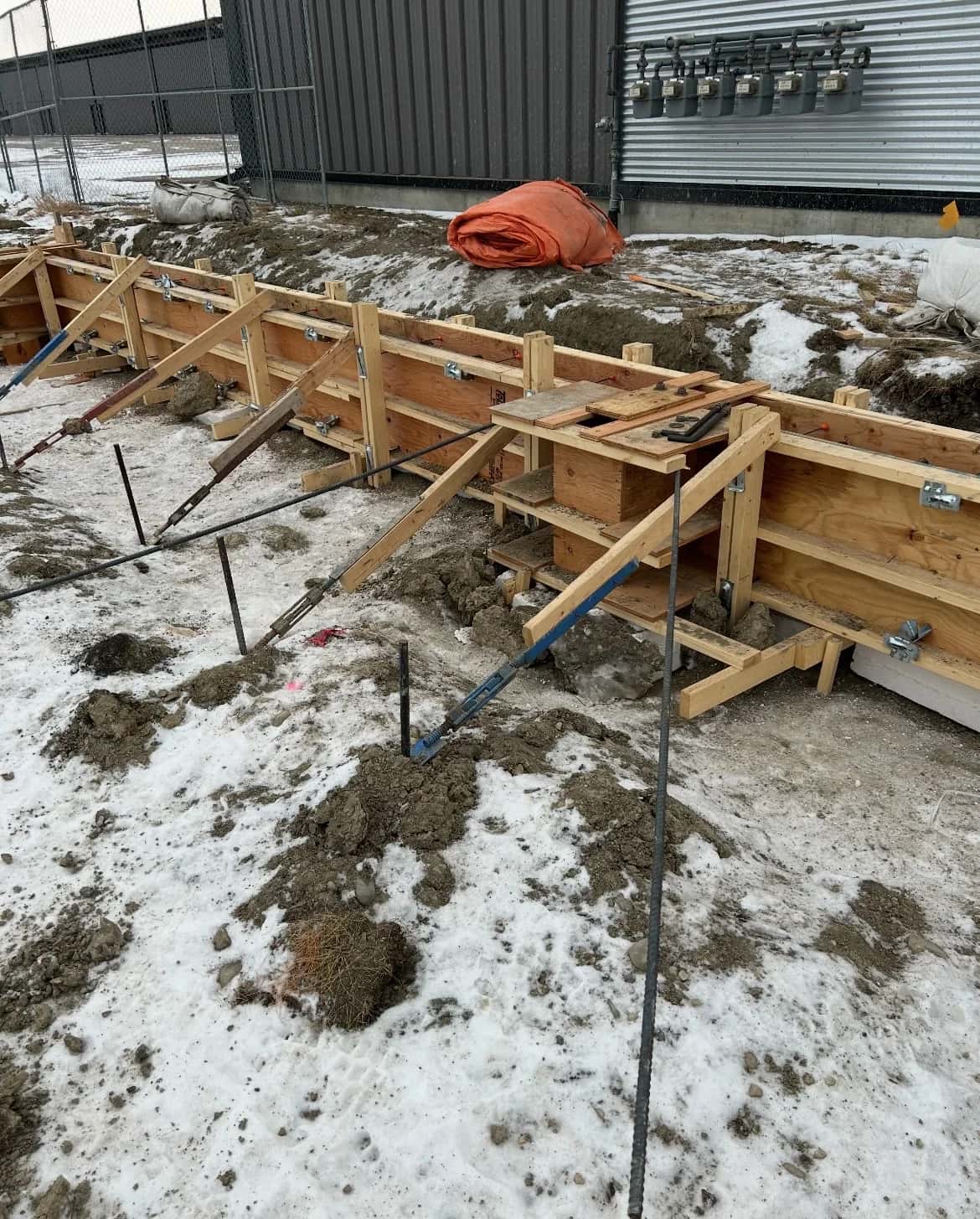 Engineered wood formwork braced with turnbuckles for a grade-beam pour beside a row of gas meters