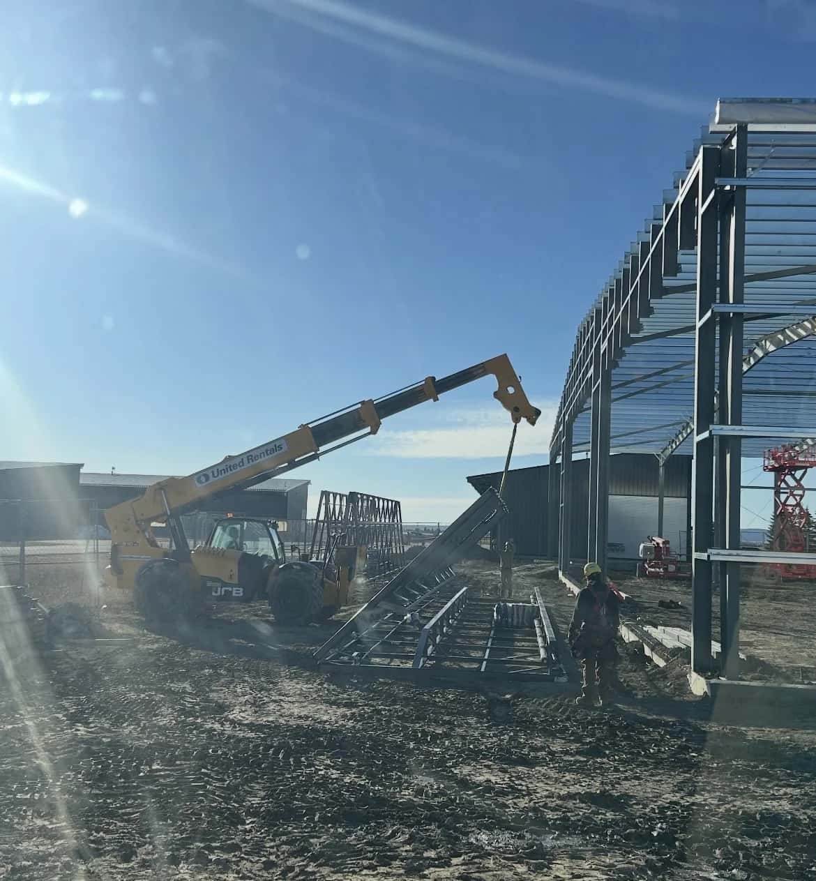 Telehandler flying a steel stair assembly with a harnessed worker guiding it into place