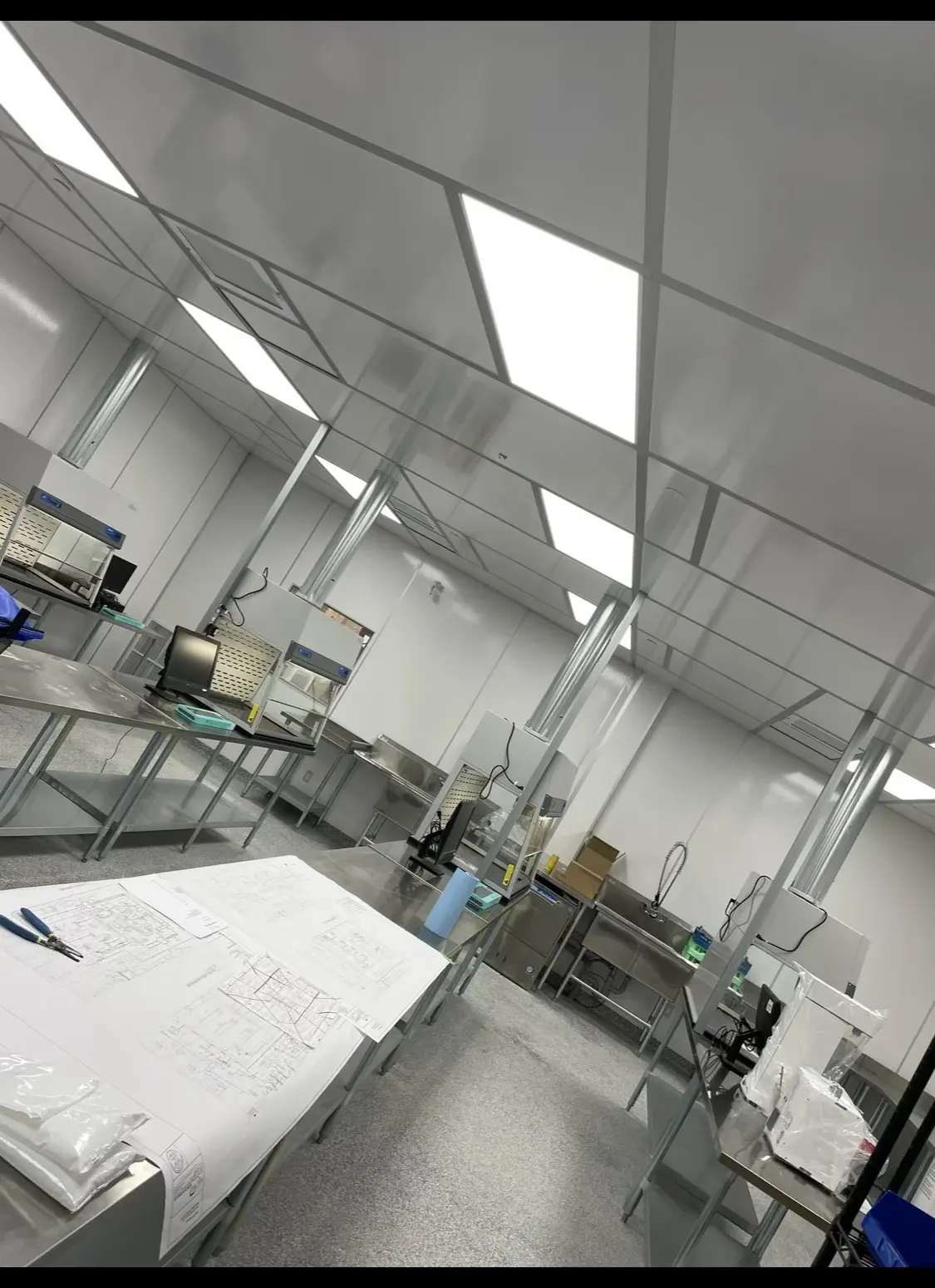 Cleanroom fit-out in progress with stainless benches, fume hoods and drawings on the table