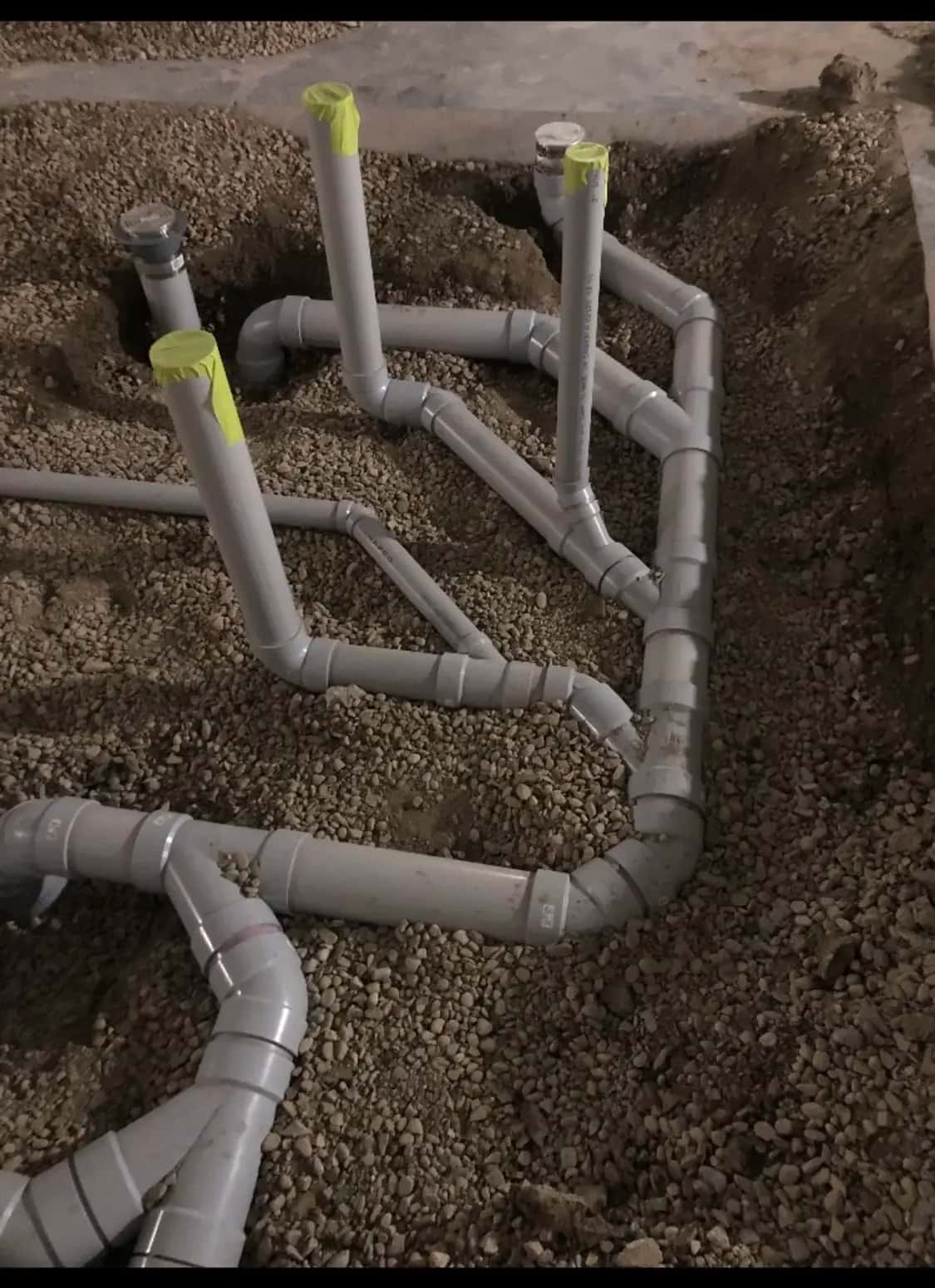 Underground PVC drainage rough-in taped off in gravel before the slab pour