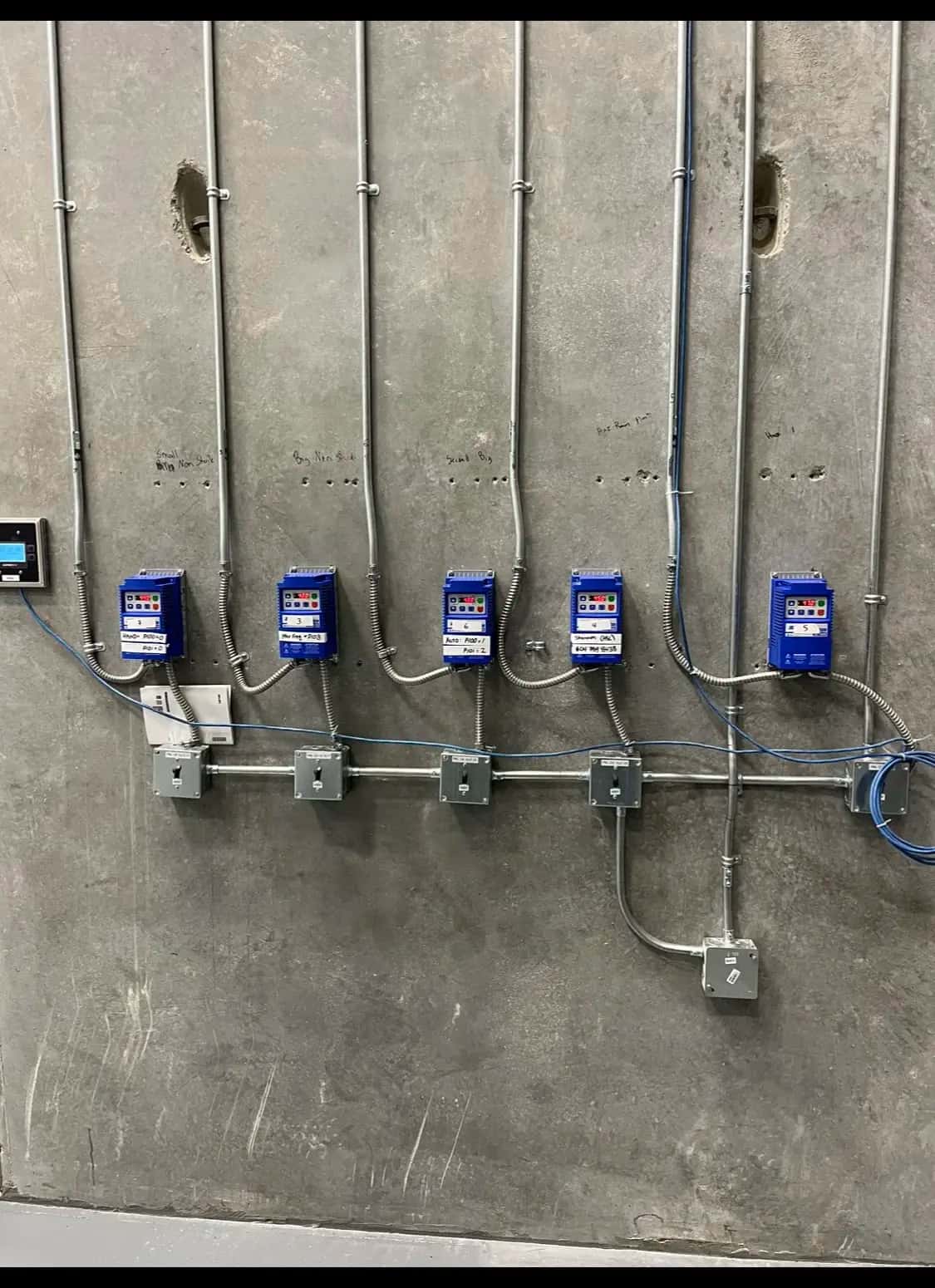 Row of labelled variable-frequency drives with conduit runs on a concrete wall