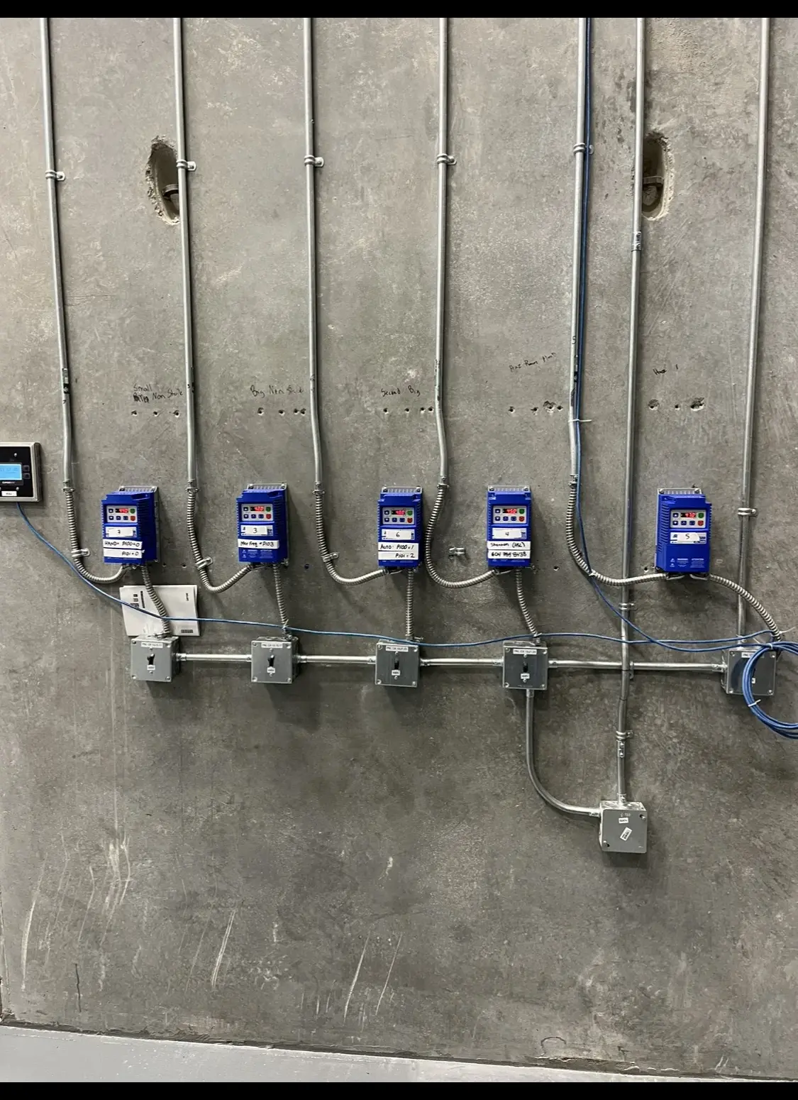 Row of labelled variable-frequency drives with conduit runs on a concrete wall