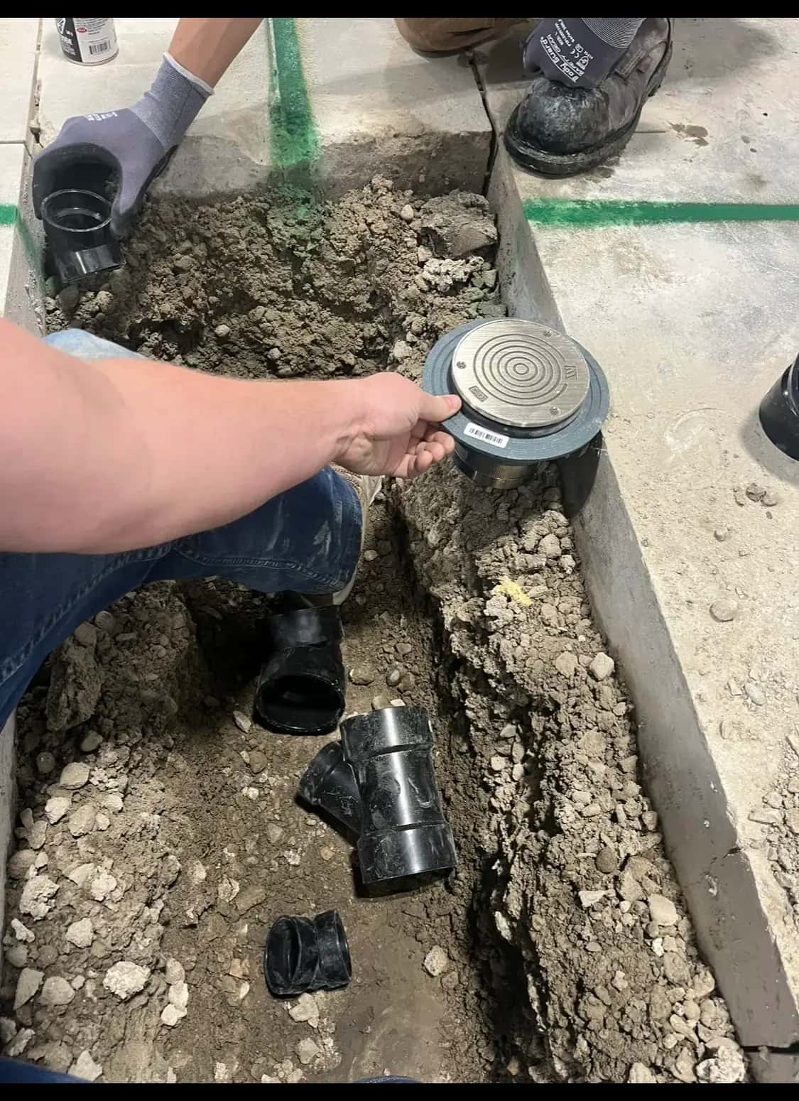 Plumber setting a stainless floor drain into a saw-cut slab trench