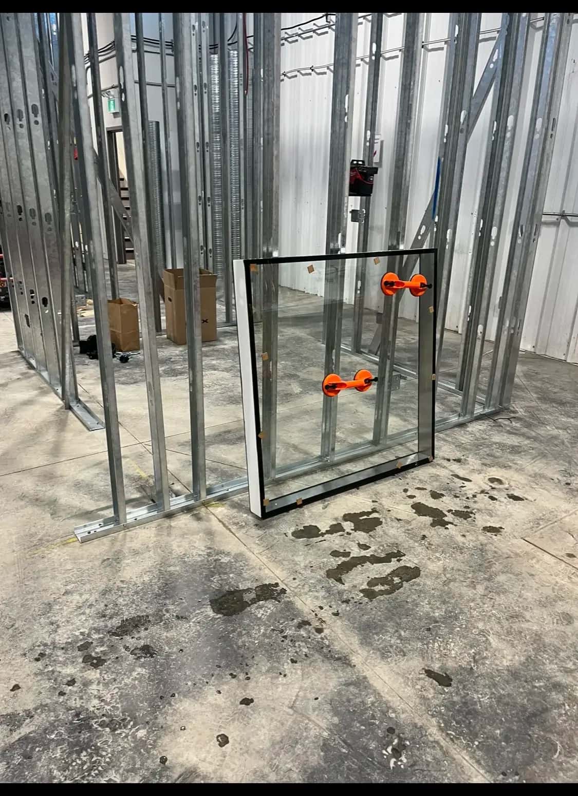 Steel-stud framing with a sealed glazing unit staged on suction-cup lifters