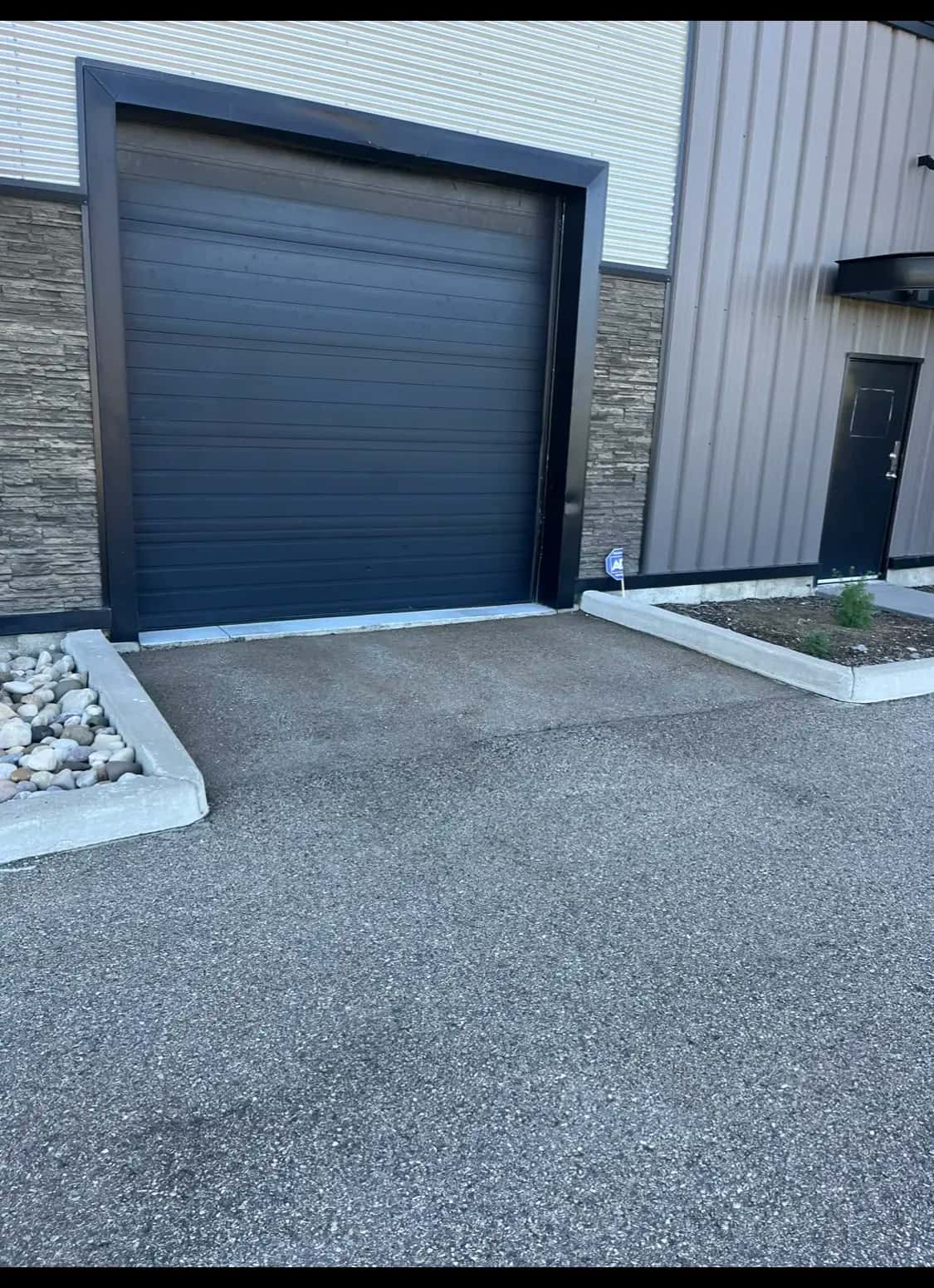 Black overhead door framed by stone veneer and metal cladding on a commercial bay